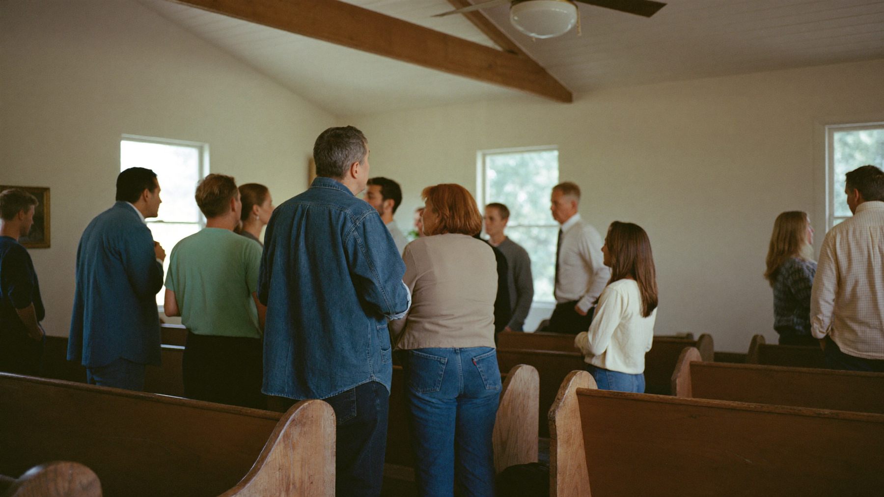 Members of a small congregation talking together between wooden pews after a service.