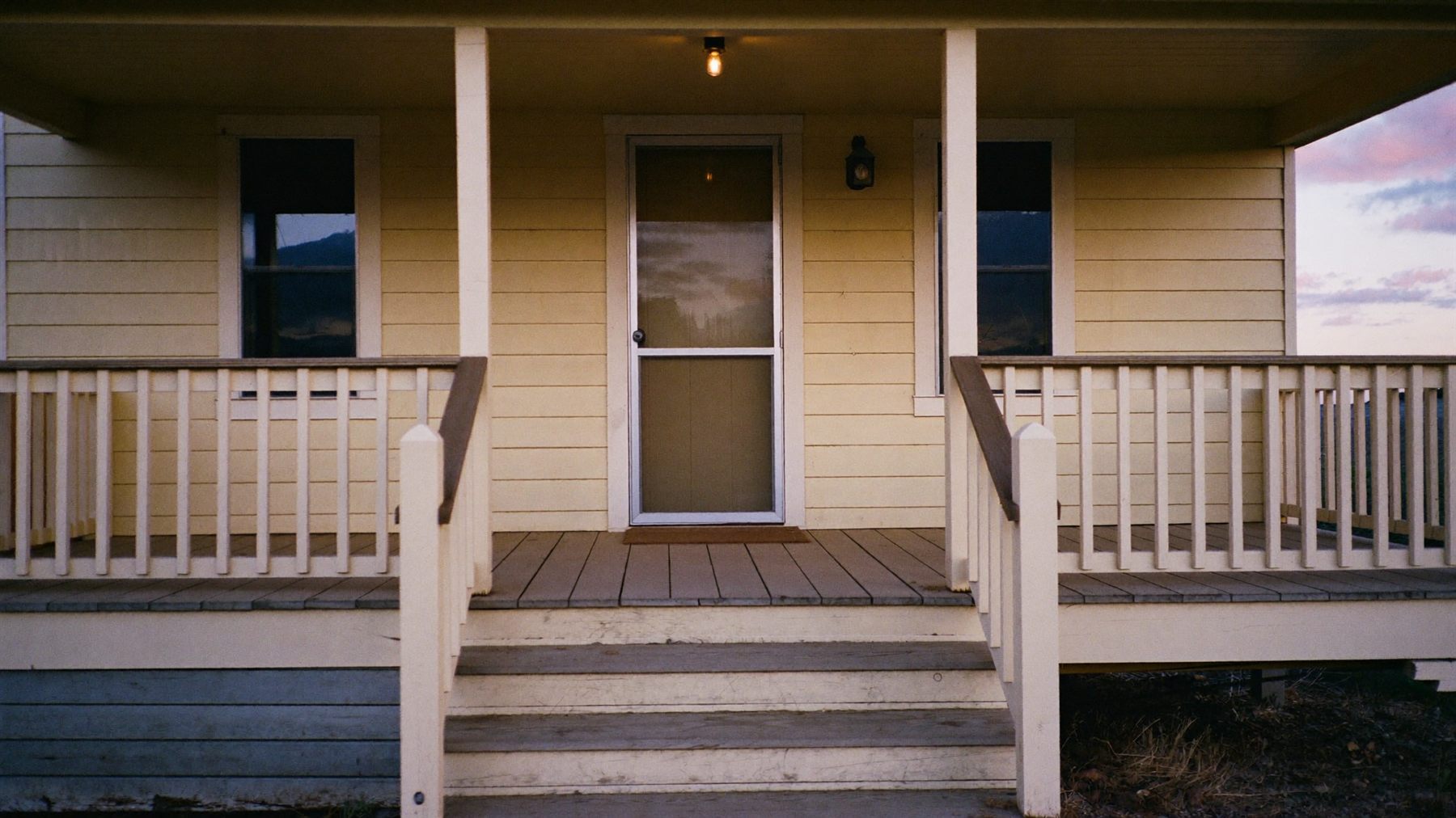 Worn wooden porch steps leading up to a screen door in warm evening light.